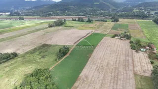 Vista aérea de uma propriedade rural com campos cultivados e vegetação no fundo.