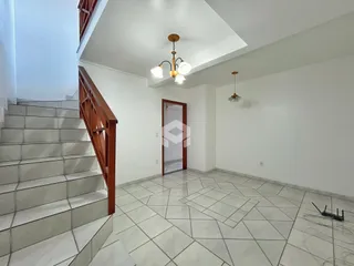 Vista de um corredor com escadaria e piso de cerâmica em uma residência.