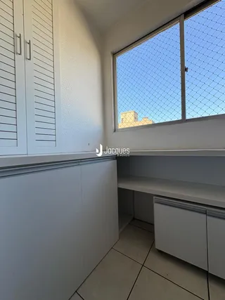 Vista interna de um cômodo com armários brancos e janela com tela de proteção.