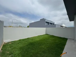 Vista externa de uma casa moderna com um gramado verde e muro branco.