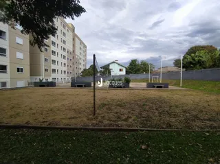 Vista externa de um terreno gramado com construções residenciais ao fundo.