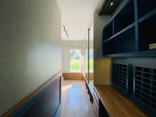 Corredor interno de uma residência com piso de madeira clara e paredes claras.