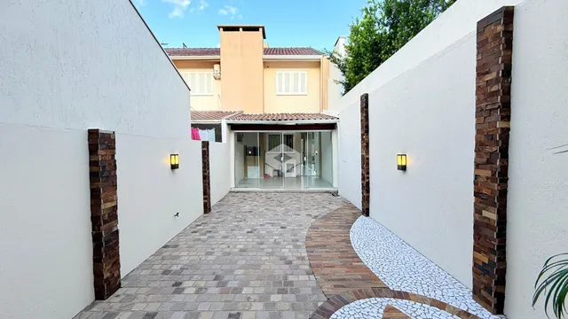 Vista da fachada de uma residência com parede branca e pilares de tijolo aparente.