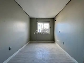 Corredor interno com paredes cinzas e piso de madeira clara, com uma janela de vista urbana.
