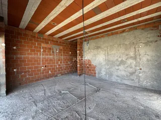 Interior de uma área em construção com paredes de tijolo aparente e piso de concreto.
