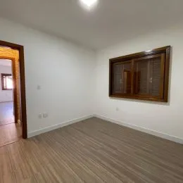 Foto interna de um cômodo com paredes brancas e piso de madeira clara.