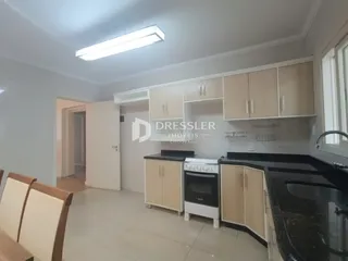 Vista interna de uma cozinha com armários claros e bancadas escuras.