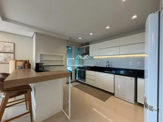 Cozinha moderna com armários brancos e bancada escura em um apartamento no Brasil.