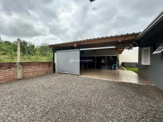 Fachada externa de uma residência com área coberta e piso de cascalho.