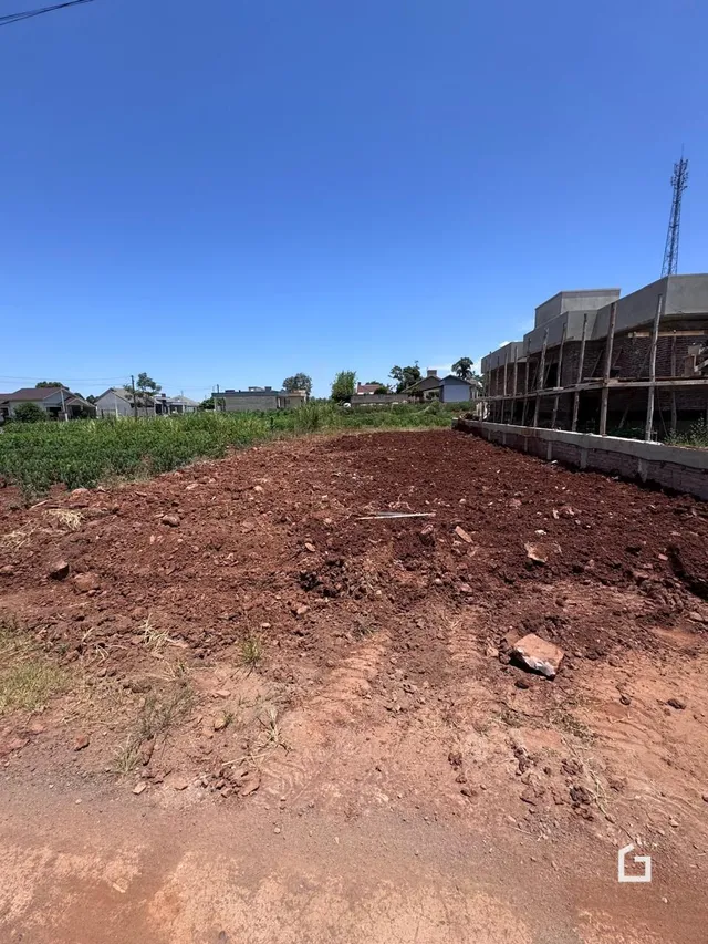 Terreno com terra avermelhada e vegetação rasteira sob céu azul.