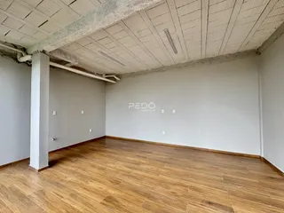 Interior de uma sala com piso de madeira e teto de concreto aparente.