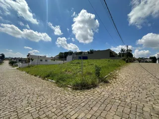 Vista externa de um terreno com pavimento de paralelepípedos e área gramada sob um céu azul.