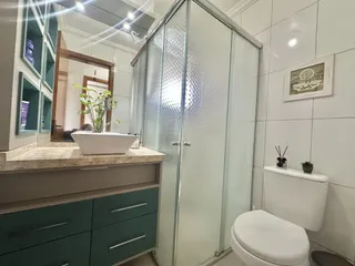 Banheiro com bancada de mármore e box de vidro transparente.