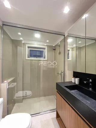 Um banheiro moderno com box de vidro e louças brancas.