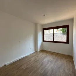 Vista interna de um cômodo com piso de madeira clara e paredes brancas.