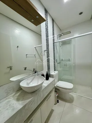 Banheiro moderno com bancada de mármore e box de vidro.