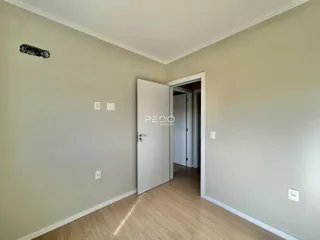 Ambiente interno de uma sala com piso de madeira clara e paredes bege.