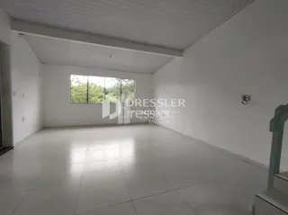 Ambiente interno de uma sala ampla com piso claro e teto branco.
