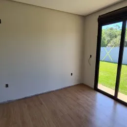 Vista interna de um cômodo com piso de madeira e parede branca.