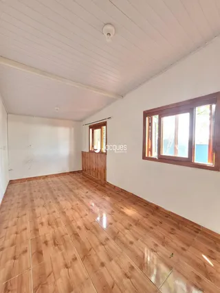 Vista interna de uma sala com piso de madeira e parede branca.