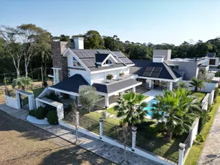 Fachada de uma casa moderna com telhado escuro e painéis solares, exibindo uma piscina no quintal.