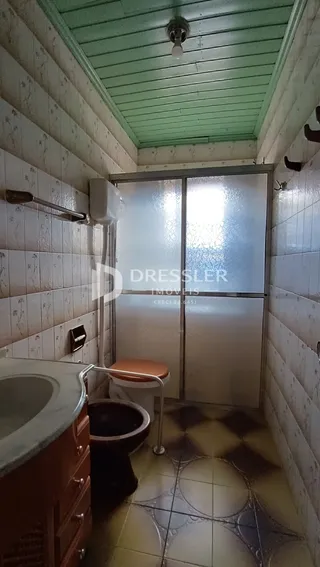 Interior de um banheiro com revestimento de azulejos brancos e piso de cerâmica.