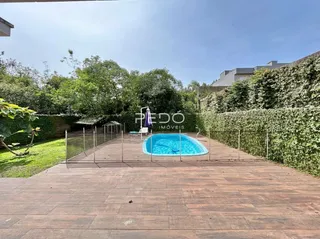 Piscina externa com deck de madeira e vegetação ao fundo.