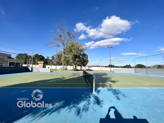 Vista aérea de uma quadra esportiva externa com rede e gramado sob um céu azul.