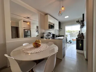 Vista de uma sala de jantar integrada à cozinha com armários brancos.