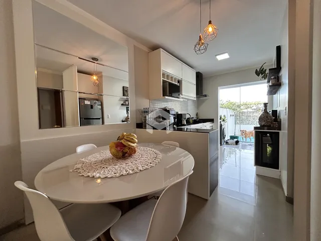 Vista de uma sala de jantar integrada à cozinha com armários brancos.