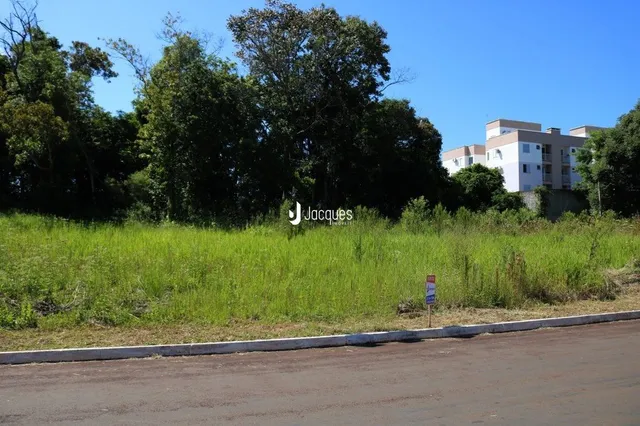 Campo gramado com vegetação e árvores ao fundo.