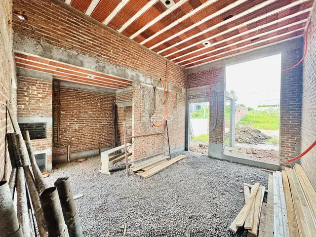 Interior de uma área em construção com paredes de tijolo aparente e piso de cascalho.
