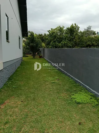Vista da fachada de uma propriedade com gramado e muro de contenção.