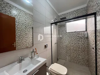 Interior de um banheiro com revestimento cerâmico e box de vidro.