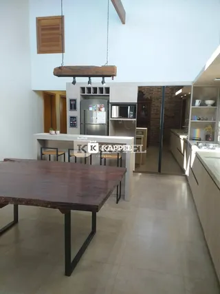 Vista interna de uma cozinha com bancadas e mesa de madeira.