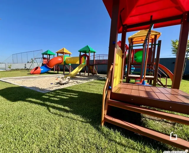 Área externa com playground e gramado em um dia ensolarado.