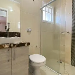 Foto de um banheiro com box de vidro e revestimento claro.