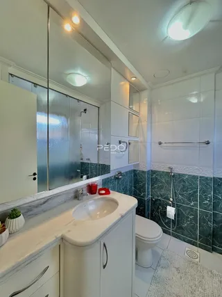 Banheiro com revestimento em azulejos verde-água e bancada branca.