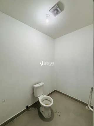 Ambiente interno com vaso sanitário branco nas paredes brancas.