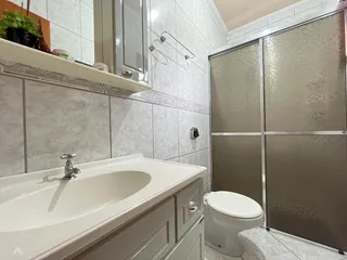Banheiro com bancada branca e box de vidro.