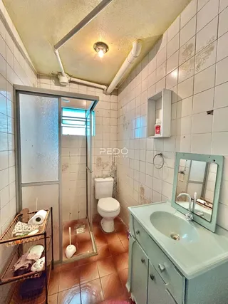 Banheiro com revestimento de azulejos brancos e piso de cerâmica marrom.