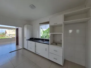 Vista da cozinha com armários brancos e piso claro em imóvel no Brasil.