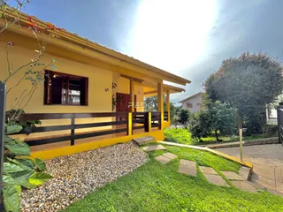 Fachada de uma casa amarela em Lajeado com jardim e muro de madeira.
