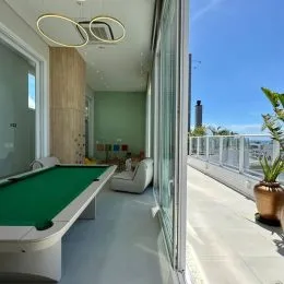 Ambiente interno com mesa de tênis de mesa e vista externa através de grandes portas de vidro.