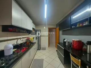 Vista interna de uma cozinha com armários brancos e escuros e piso de cerâmica.