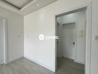 Foto de um corredor interno com paredes brancas e piso de madeira clara.