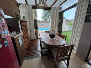 Área de jantar com mesa de madeira e acesso a um pátio com piscina.