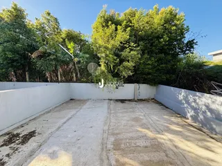 Vista de um pátio externo cercado por um muro branco e vegetação densa.