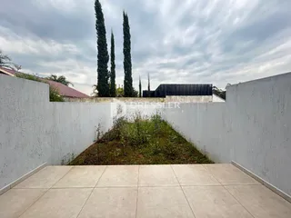 Vista externa de um pátio com muro branco e jardim.