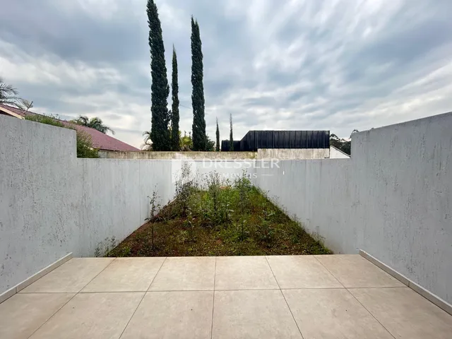 Vista externa de um pátio com muro branco e jardim.